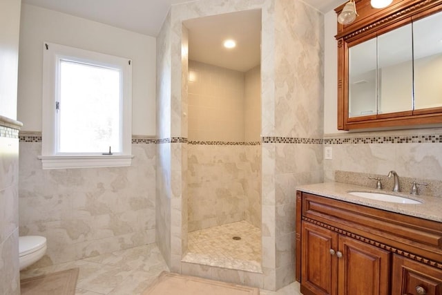 bathroom featuring vanity, toilet, tiled shower, and tile walls