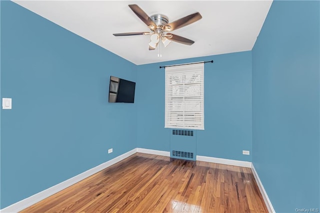 spare room featuring ceiling fan, radiator heating unit, wood finished floors, and baseboards