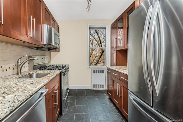 kitchen featuring stainless steel appliances, decorative backsplash, glass insert cabinets, a sink, and light stone countertops