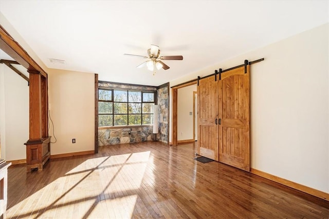 spare room featuring a barn door, ceiling fan, and wood-type flooring