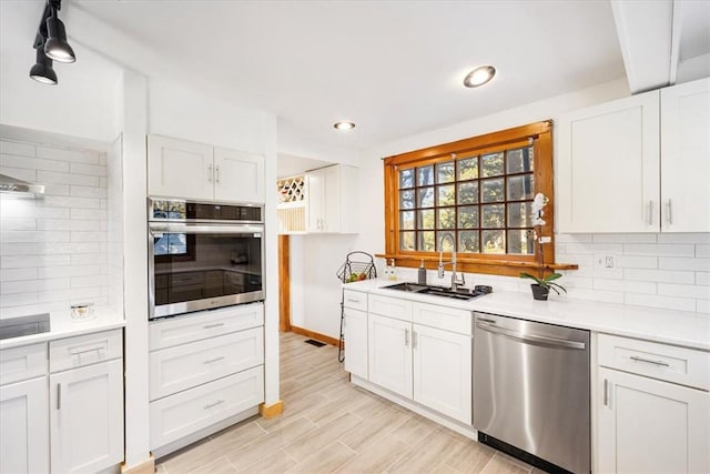 kitchen featuring white cabinetry, sink, stainless steel appliances, backsplash, and light wood-type flooring