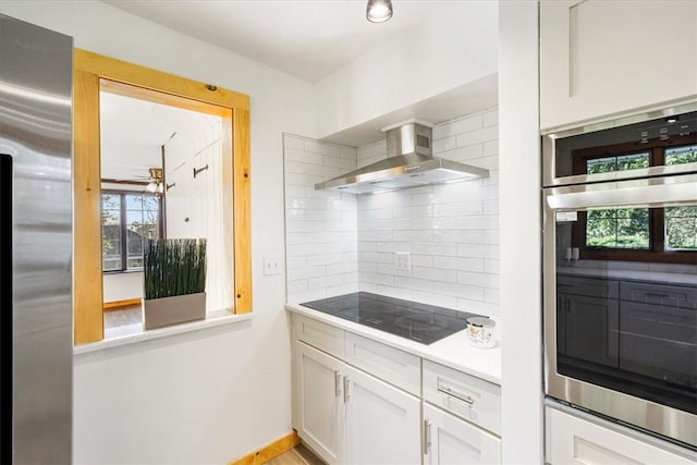 kitchen featuring decorative backsplash, white cabinetry, wall chimney exhaust hood, and stainless steel appliances