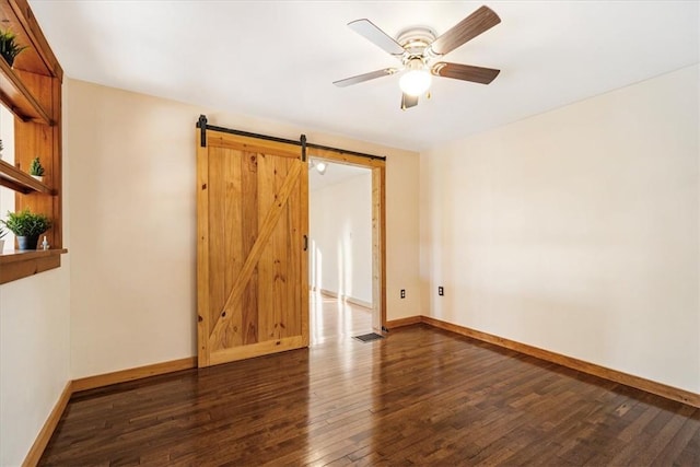 empty room with a barn door, dark hardwood / wood-style floors, and ceiling fan