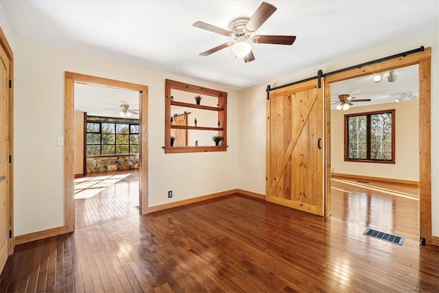 empty room with hardwood / wood-style floors, ceiling fan, and a barn door