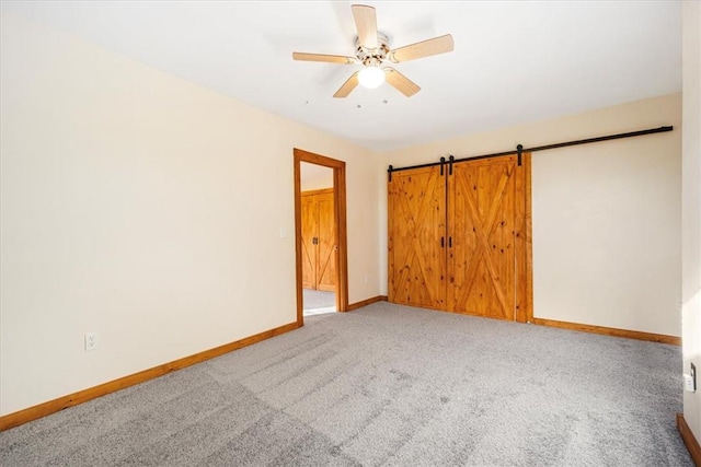 spare room featuring carpet, a barn door, and ceiling fan