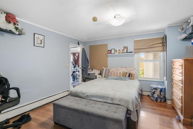 bedroom featuring hardwood / wood-style floors, ornamental molding, and a baseboard heating unit