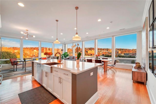 kitchen with light wood-type flooring, sink, pendant lighting, white cabinets, and an island with sink