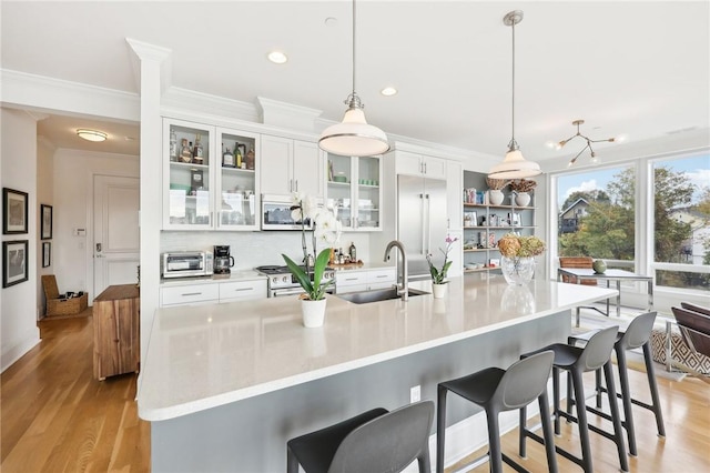 kitchen with white cabinets, pendant lighting, stainless steel appliances, and light hardwood / wood-style flooring