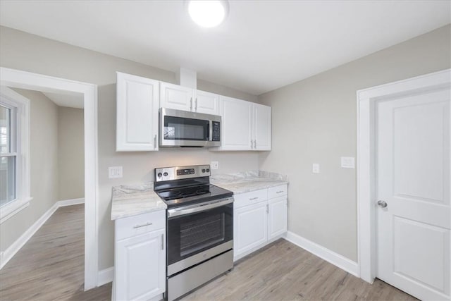 kitchen with light stone countertops, white cabinetry, stainless steel appliances, and light wood-type flooring