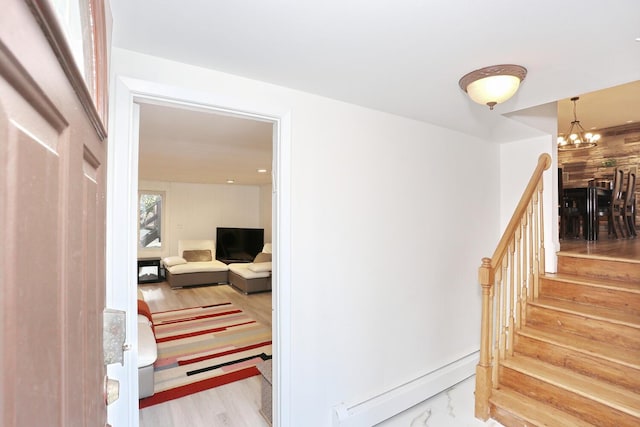 stairway with hardwood / wood-style flooring, a baseboard radiator, and a notable chandelier