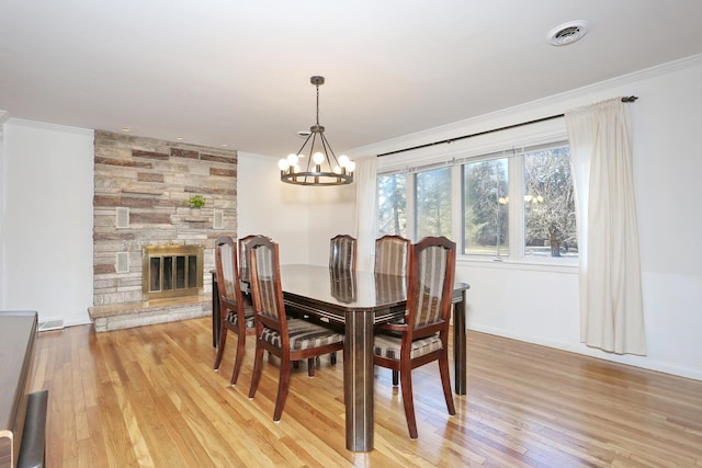 dining space with a fireplace, light hardwood / wood-style flooring, ornamental molding, and a notable chandelier