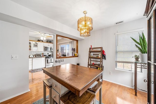 dining space with ceiling fan with notable chandelier and light hardwood / wood-style flooring