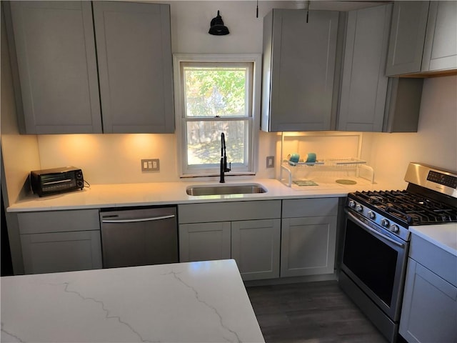 kitchen featuring gray cabinets, appliances with stainless steel finishes, dark hardwood / wood-style floors, sink, and light stone counters