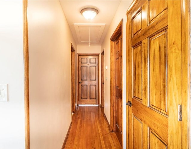 hallway featuring attic access, baseboards, and light wood finished floors