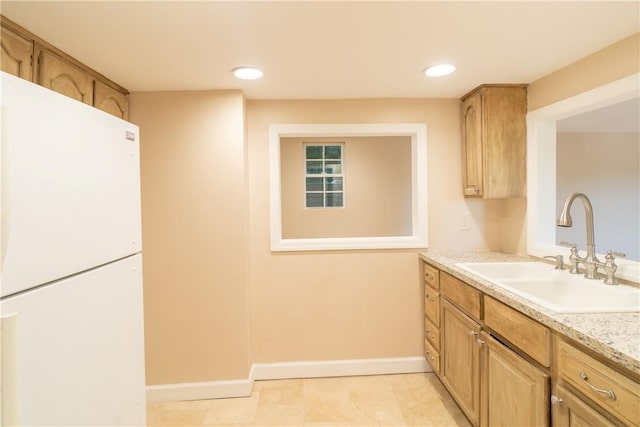 kitchen with light brown cabinets, a sink, freestanding refrigerator, and baseboards