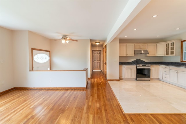 kitchen with dark countertops, light wood-style floors, gas stove, under cabinet range hood, and baseboards