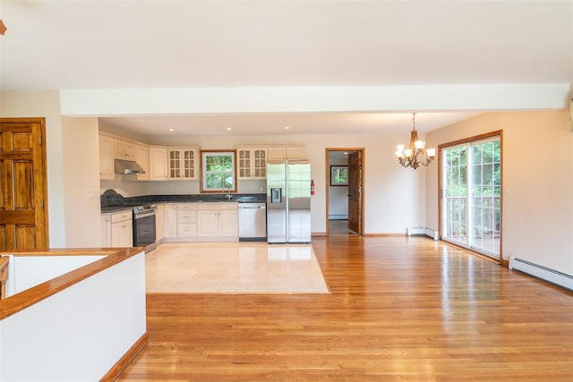 kitchen with under cabinet range hood, stainless steel appliances, hanging light fixtures, dark countertops, and glass insert cabinets