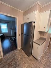 kitchen with white cabinetry, light hardwood / wood-style flooring, fridge, and ornamental molding