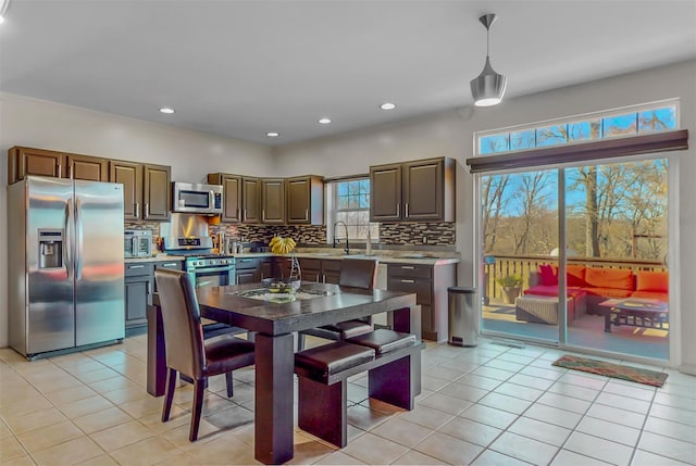 kitchen featuring sink, hanging light fixtures, decorative backsplash, light tile patterned floors, and appliances with stainless steel finishes