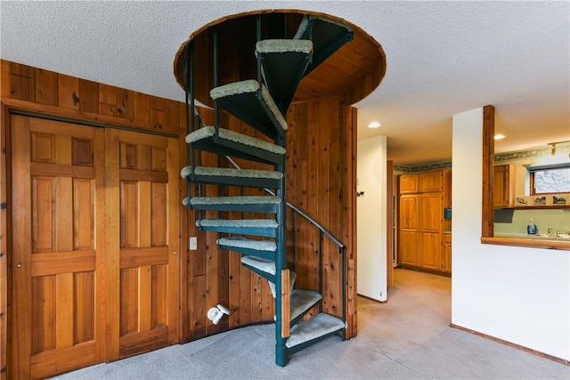 stairway with carpet, a textured ceiling, and wooden walls