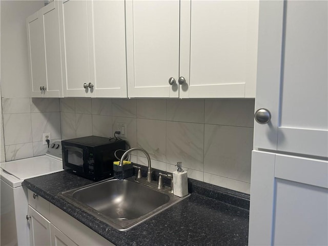 kitchen featuring tasteful backsplash, washer / clothes dryer, white cabinetry, and sink