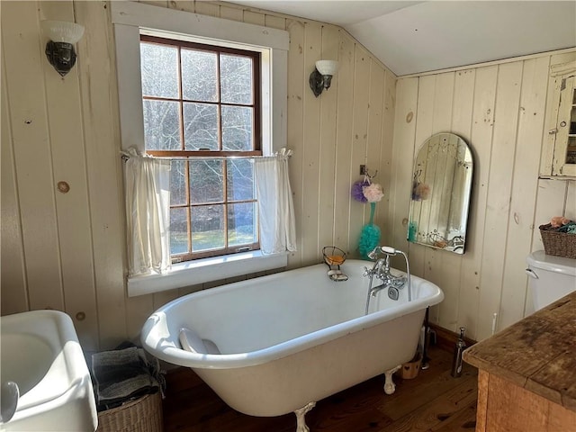 bathroom with hardwood / wood-style flooring, a washtub, wooden walls, and vaulted ceiling