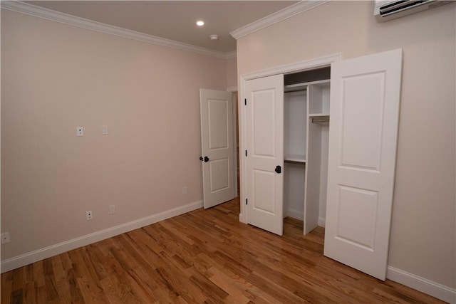 unfurnished bedroom with an AC wall unit, a closet, wood-type flooring, and ornamental molding