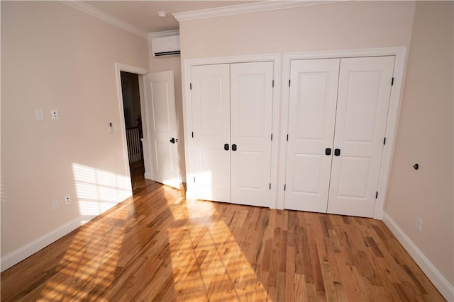 unfurnished bedroom featuring multiple closets, light hardwood / wood-style floors, a wall mounted AC, and ornamental molding