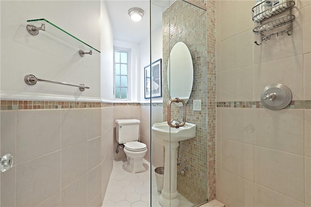 bathroom with toilet, tile walls, tiled shower, and tile patterned flooring