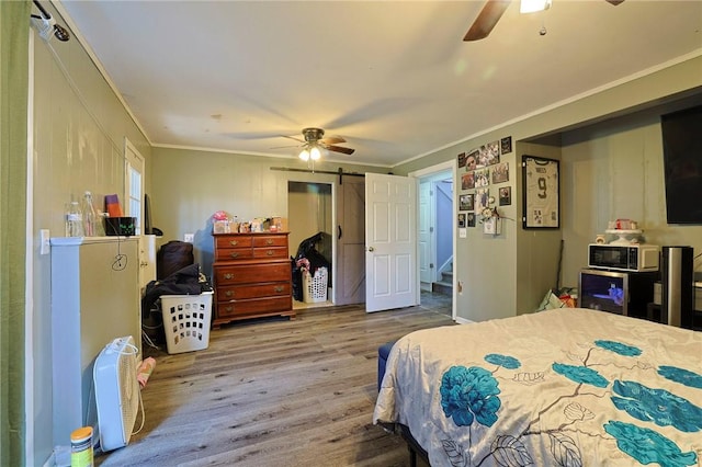 bedroom featuring hardwood / wood-style floors, a barn door, ceiling fan, and crown molding