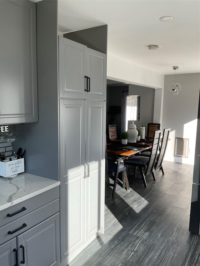 kitchen with light stone countertops, dark hardwood / wood-style flooring, hanging light fixtures, and gray cabinetry