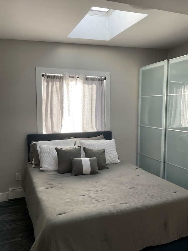 bedroom featuring a skylight, dark hardwood / wood-style floors, and a baseboard heating unit