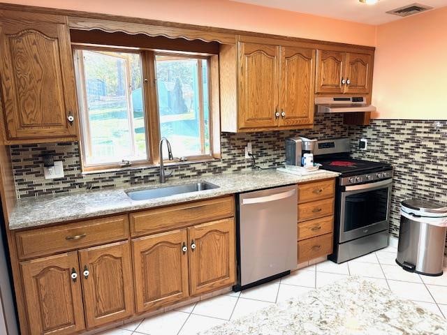 kitchen with backsplash, stainless steel appliances, light stone counters, and sink