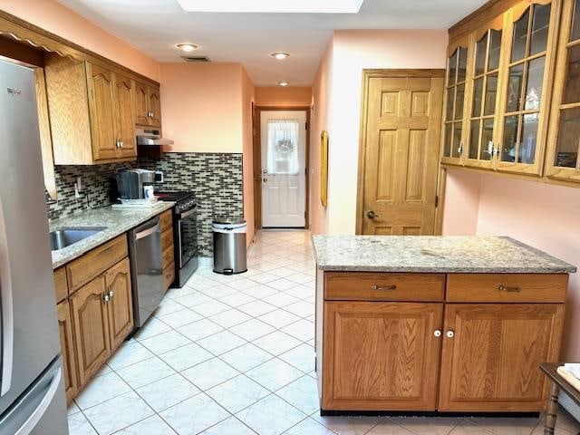 kitchen with decorative backsplash, appliances with stainless steel finishes, a skylight, and light stone counters