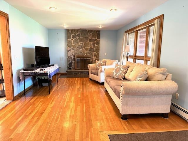 living room featuring a stone fireplace, wood-type flooring, and a baseboard radiator