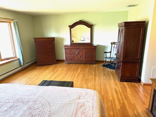 bedroom with light hardwood / wood-style floors and a baseboard radiator