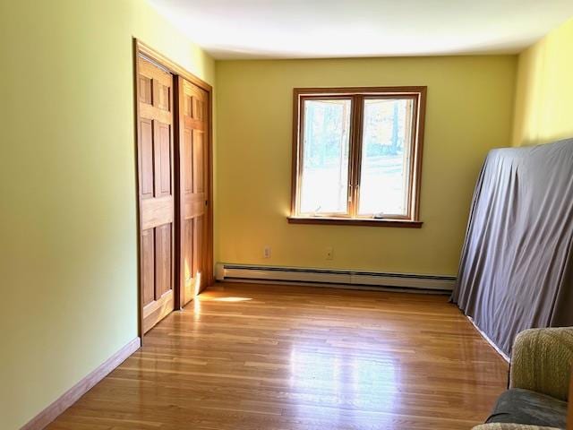 unfurnished bedroom with a closet, baseboard heating, and light hardwood / wood-style flooring