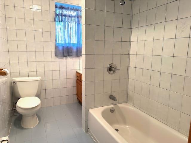 full bathroom with tile patterned floors, vanity, tiled shower / bath combo, tile walls, and toilet