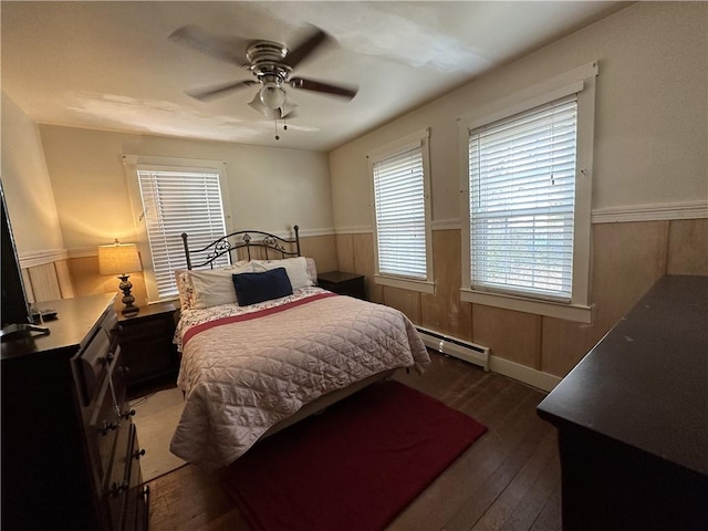 bedroom featuring ceiling fan, dark wood-type flooring, a baseboard radiator, and wooden walls