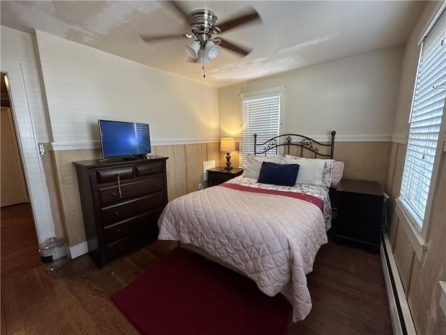 bedroom featuring dark hardwood / wood-style flooring, wooden walls, ceiling fan, and a baseboard heating unit