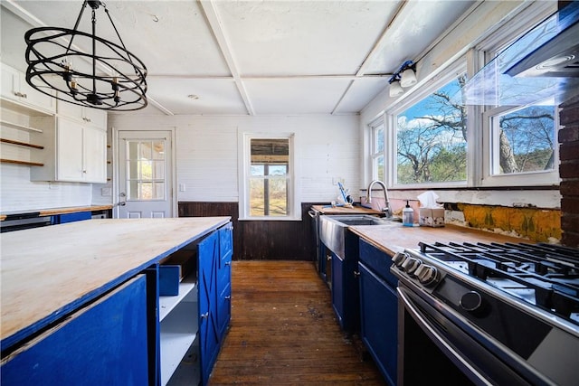 kitchen with gas range oven, blue cabinets, dark hardwood / wood-style floors, white cabinetry, and wood walls