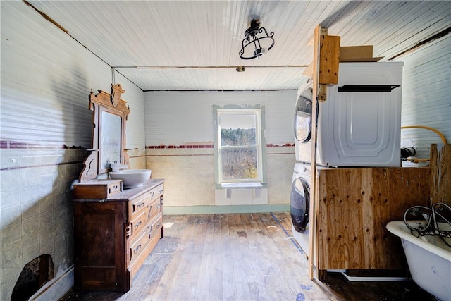 bathroom with vanity, wood walls, stacked washer and clothes dryer, hardwood / wood-style flooring, and a tub to relax in