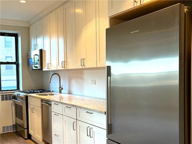 kitchen with light hardwood / wood-style floors, light stone counters, white cabinetry, and stainless steel appliances