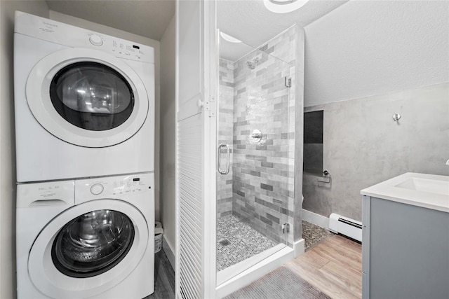 laundry area featuring wood-type flooring, a baseboard radiator, stacked washer / dryer, and sink