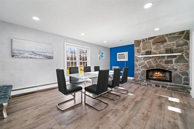 dining space featuring a fireplace, wood-type flooring, a wall mounted air conditioner, and a baseboard heating unit