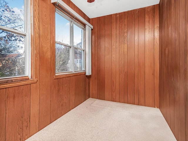 carpeted empty room with ceiling fan and wood walls