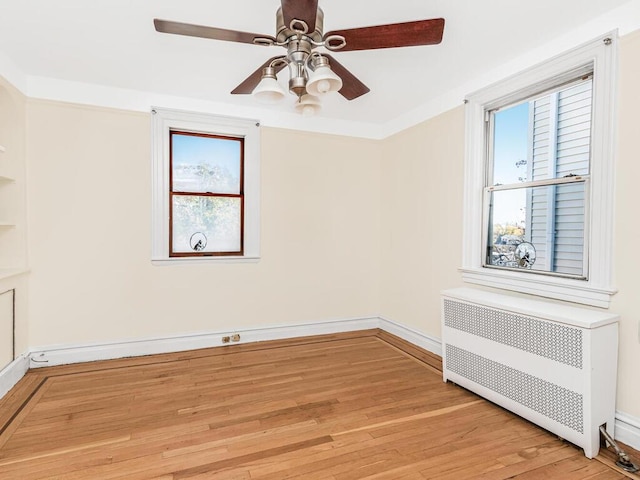 spare room with radiator heating unit, light wood-type flooring, and ceiling fan