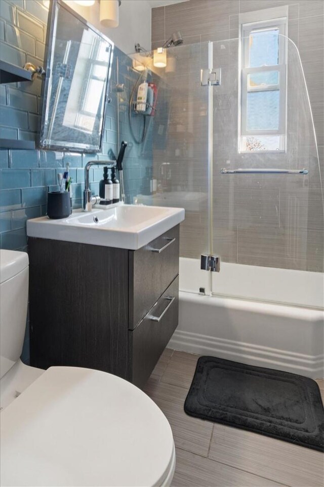 full bathroom with shower / bath combination with glass door, plenty of natural light, vanity, and tile walls