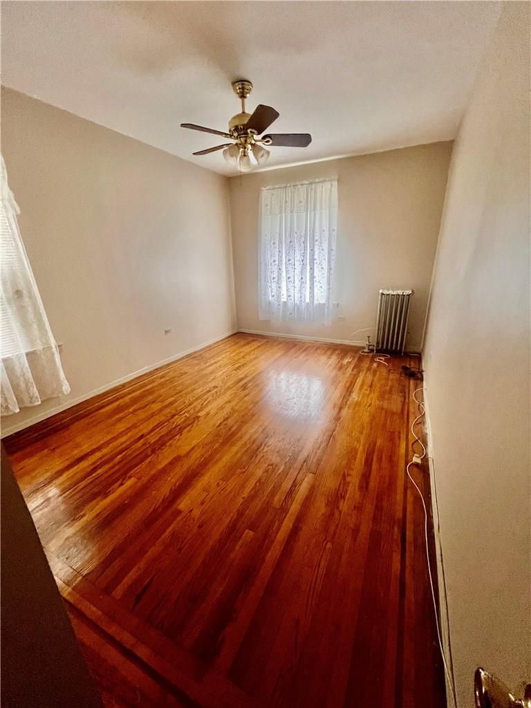 empty room with ceiling fan, hardwood / wood-style floors, and radiator heating unit