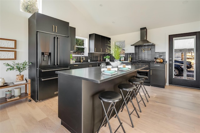 kitchen with a center island, wall chimney exhaust hood, a breakfast bar area, decorative backsplash, and high end appliances